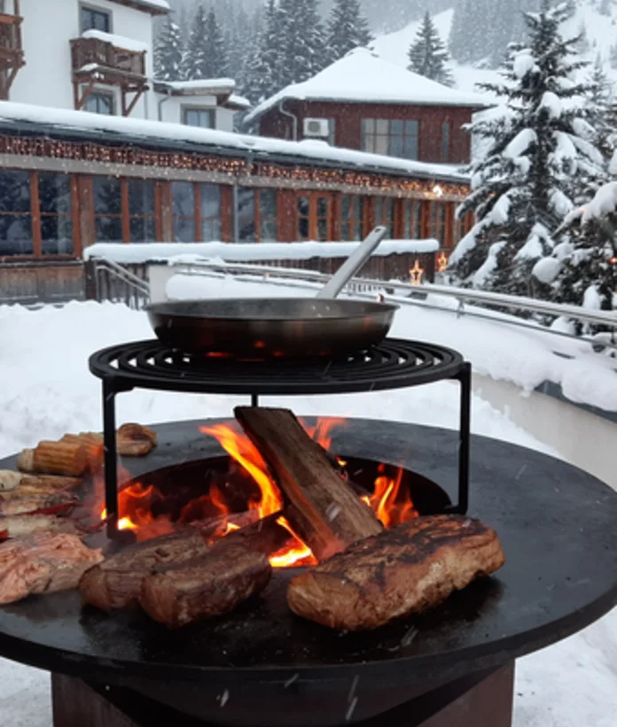 OFYR grill with meat, vegetables and pan in the snow in front of buildings