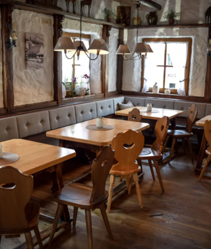 Rustic dining room with wooden tables, chairs and corner bench under subdued light
