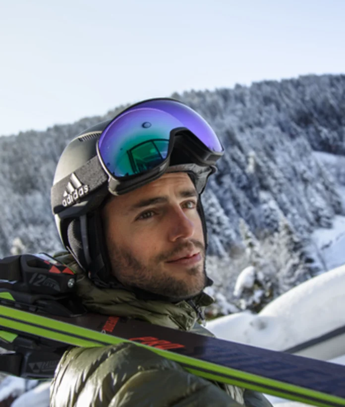 Man with ski helmet and ski goggles in front of snowy mountain landscape