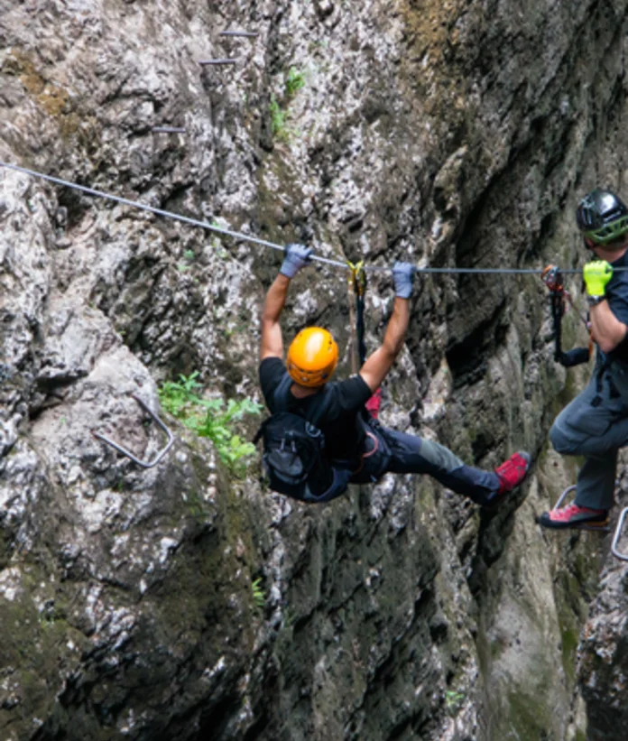 Climber on a steel cable in a steep rock face, secured by a helmet and via ferrata set